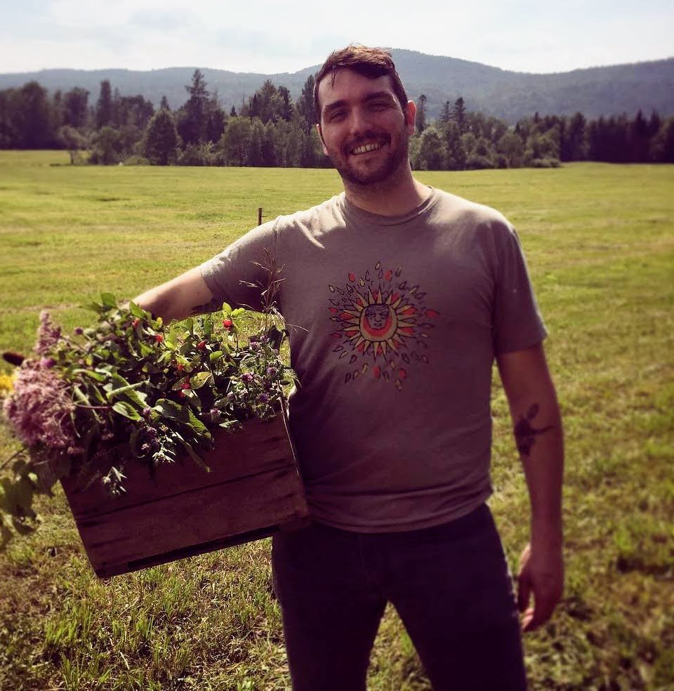 Chef Tyler Haydon holding a wooden basket of flowers in a Vermont field