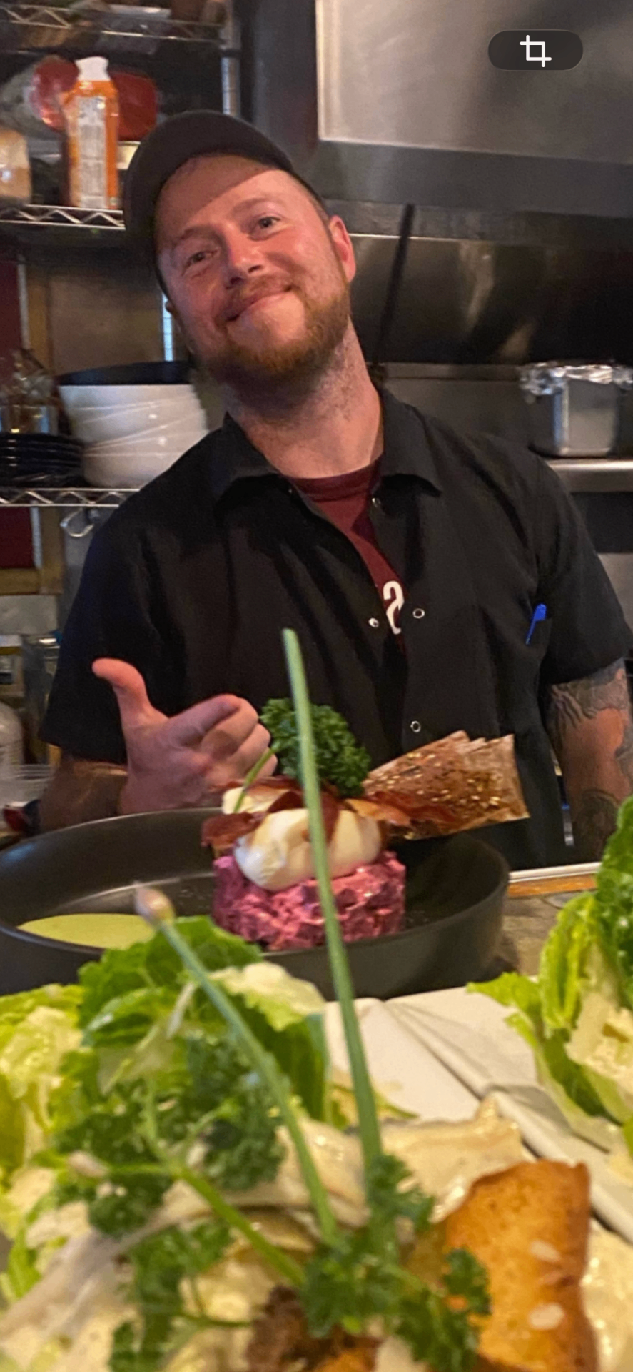 Executive Chef Jon Perdue smiling in the kitchen with a plated dish in the foreground